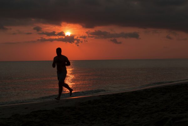 Uomo che corre sulla spiaggia al tramonto durante il caldo estivo