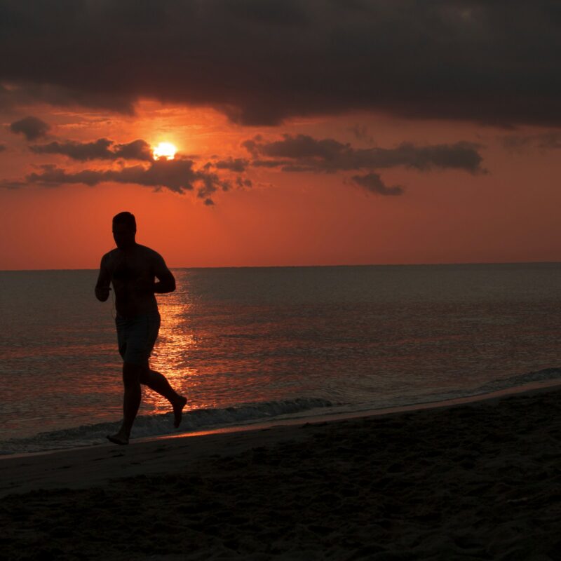 Uomo che corre sulla spiaggia al tramonto durante il caldo estivo