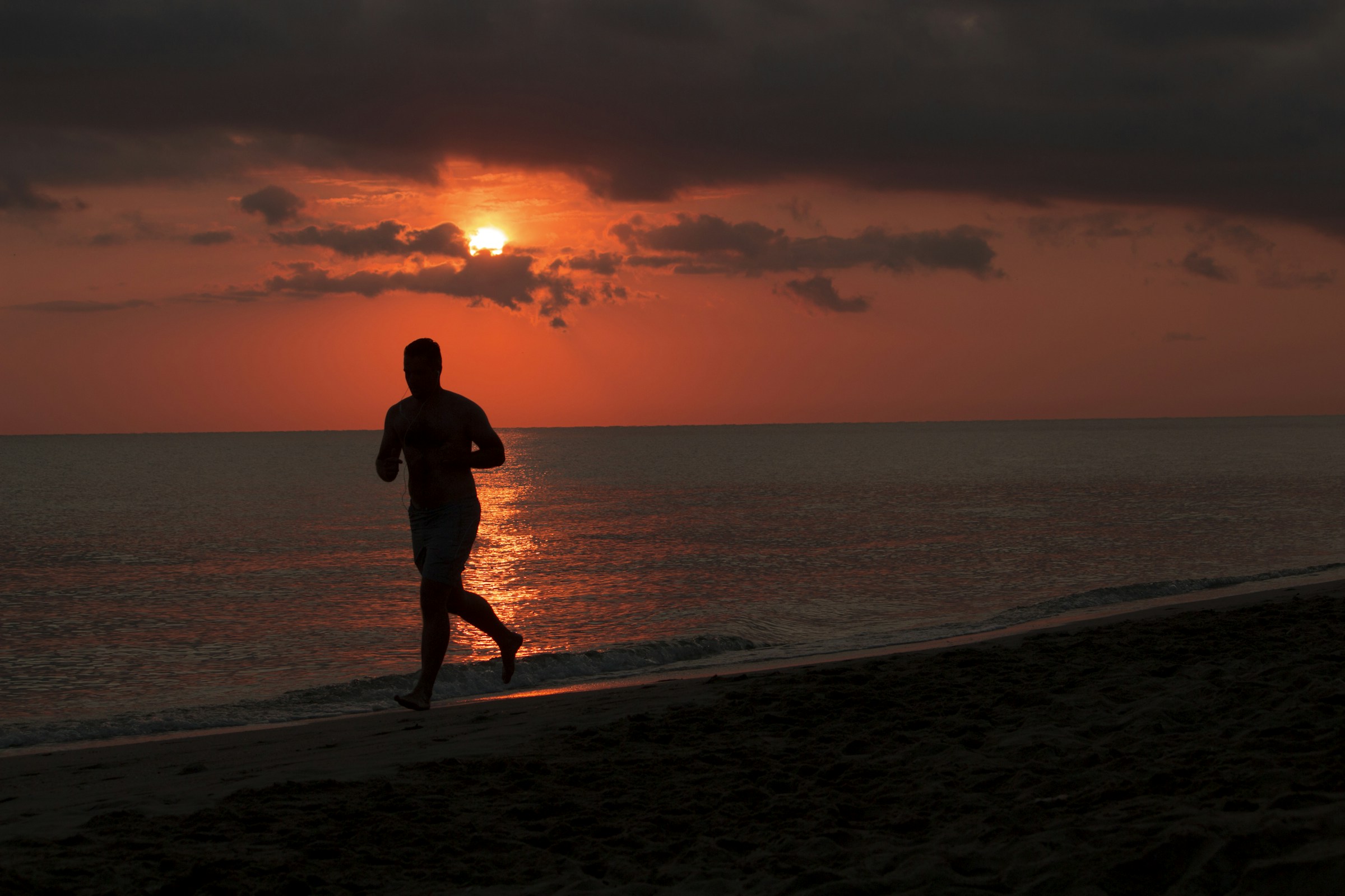 Uomo che corre sulla spiaggia al tramonto durante il caldo estivo