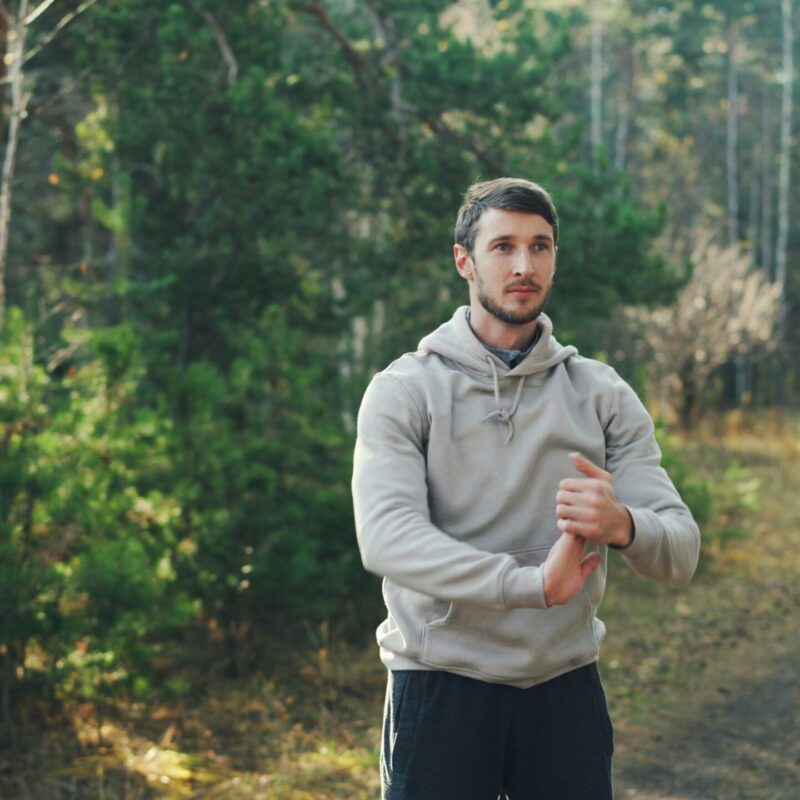 Uomo adulto attivo fa stretching all'aperto in un bosco dopo lo sport
