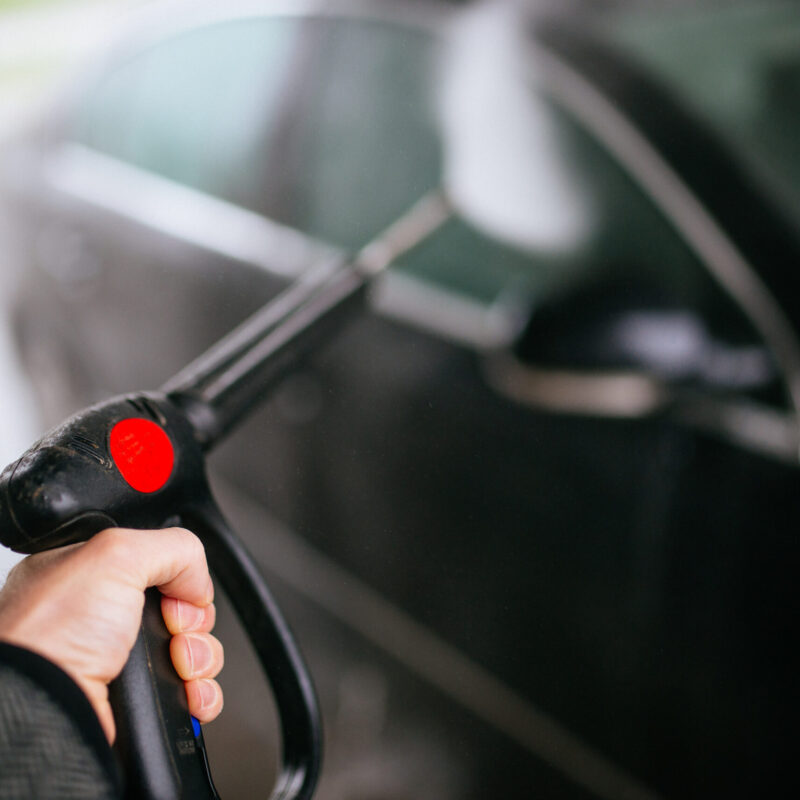 Addetto lava un'auto con idropulitrice ad alta pressione in un autolavaggio all'aperto