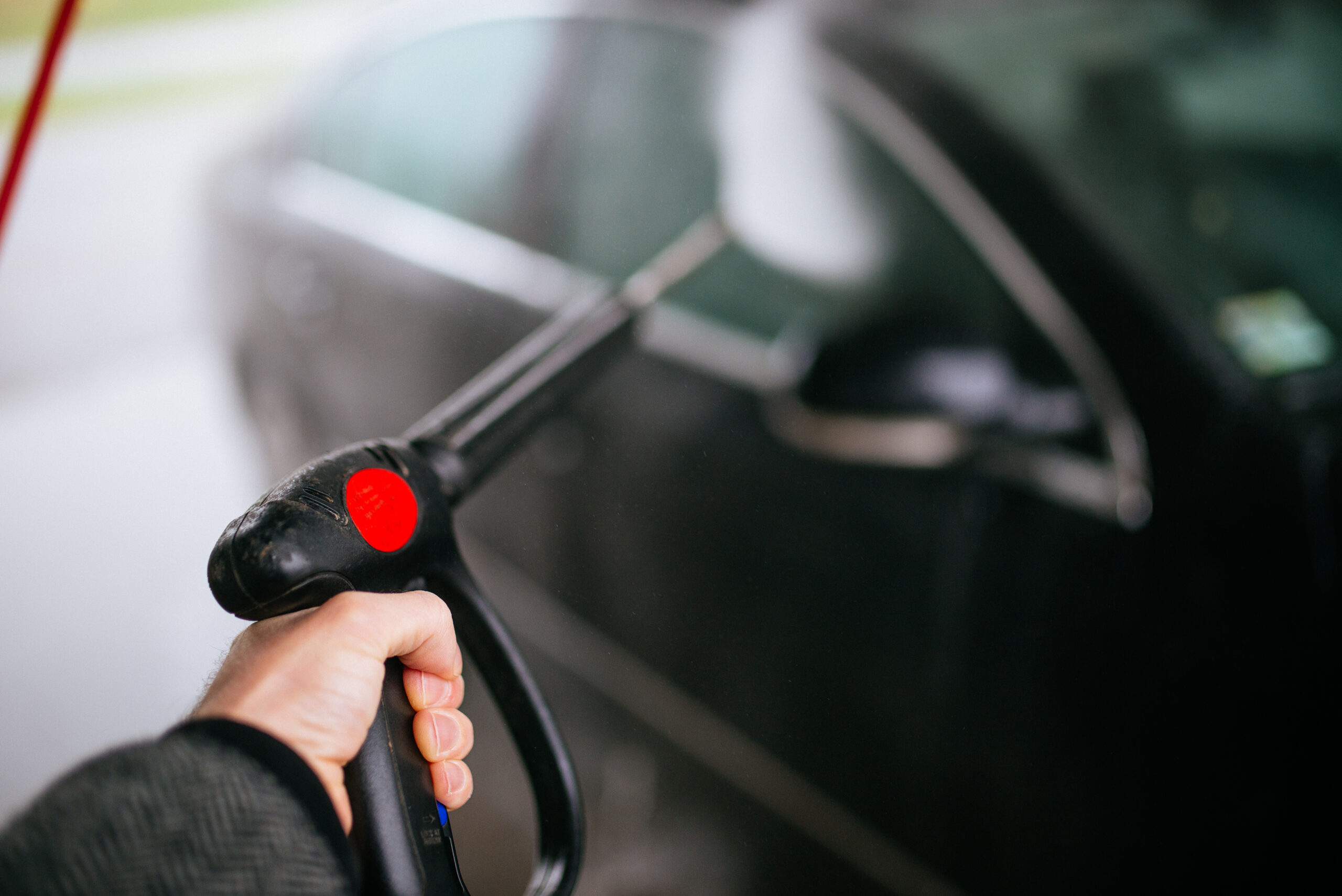 Addetto lava un'auto con idropulitrice ad alta pressione in un autolavaggio all'aperto