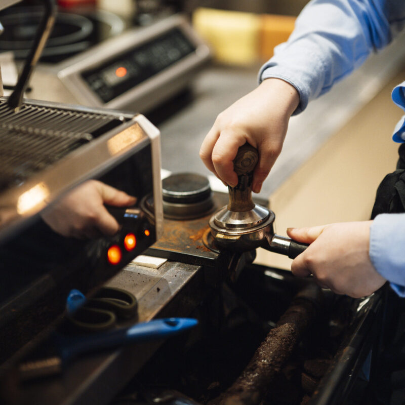 Mani di un barista che preparano un espresso con il pressino sul portafiltro