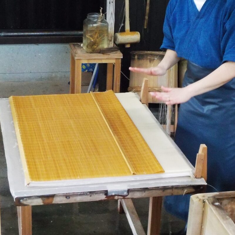 Mani di un mastro cartaio giapponese al lavoro su un telaio con schermo di bambù durante la produzione della carta washi fatta a mano