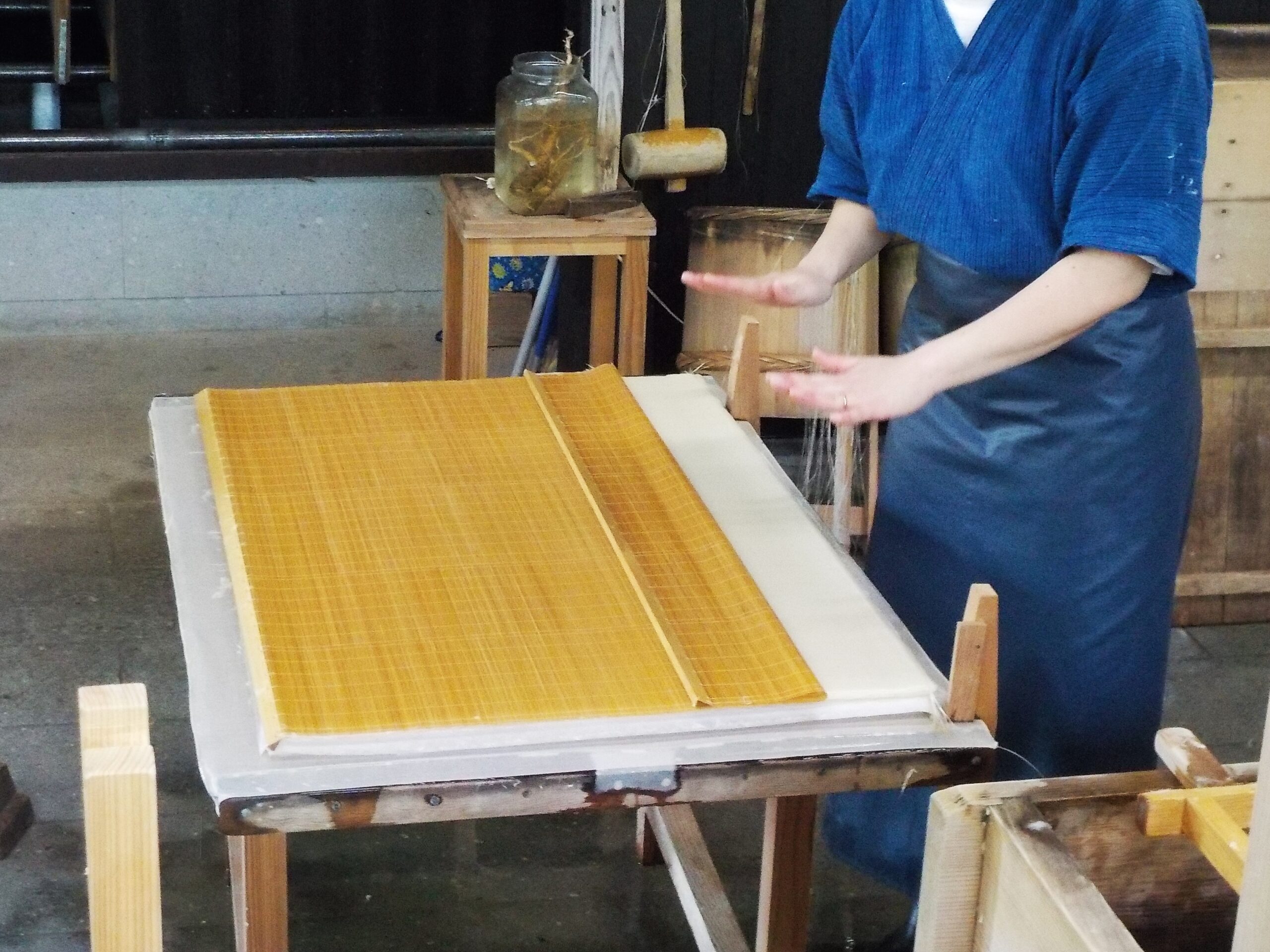 Mani di un mastro cartaio giapponese al lavoro su un telaio con schermo di bambù durante la produzione della carta washi fatta a mano