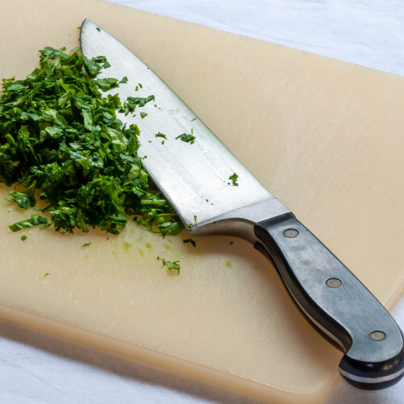 Coltello da cucina professionale con erbe aromatiche tritate su tagliere