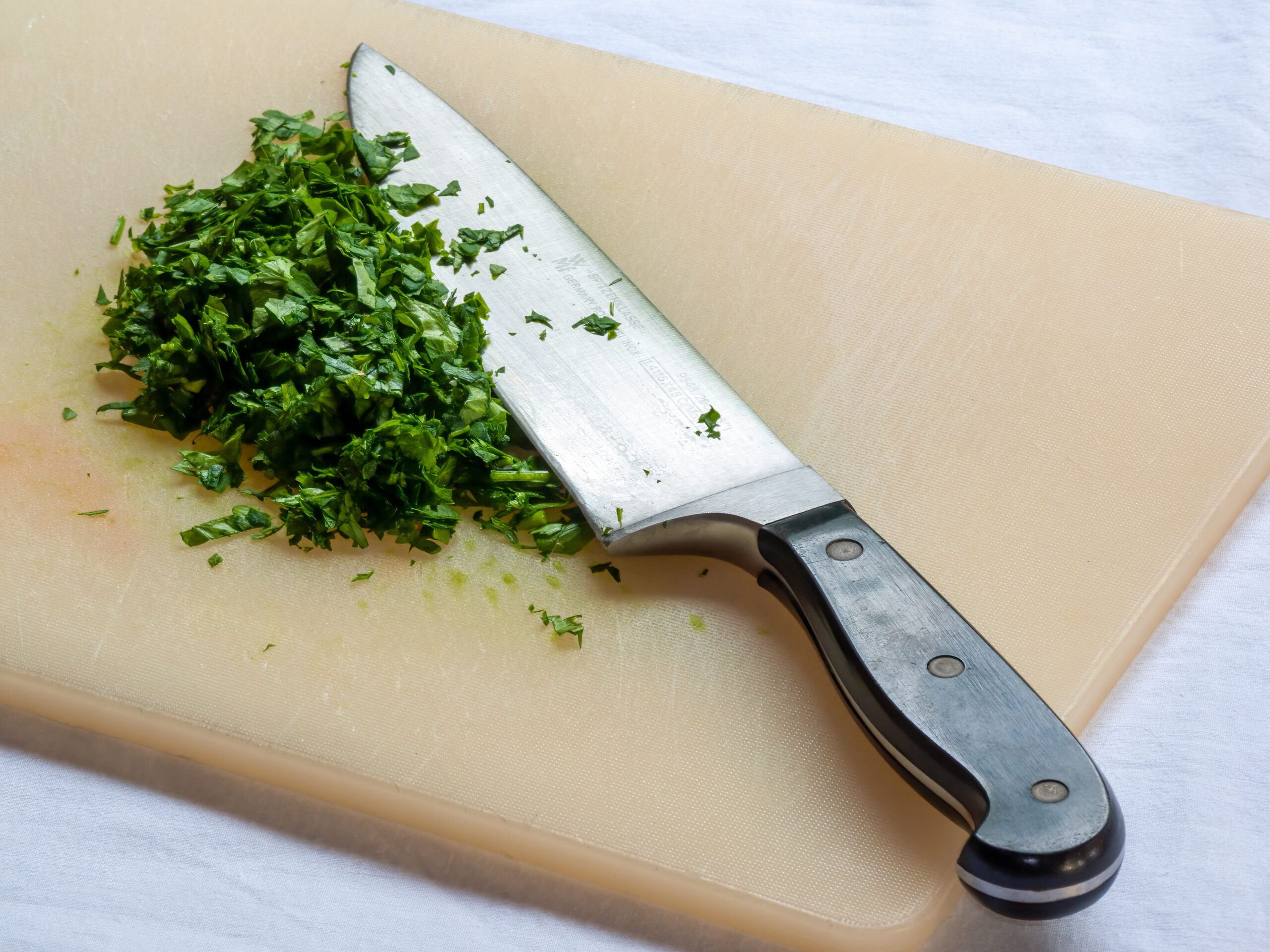 Coltello da cucina professionale con erbe aromatiche tritate su tagliere