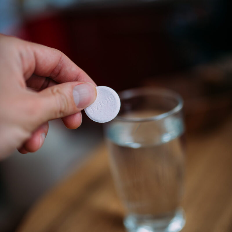 Persona tiene una compressa effervescente sopra un bicchiere d'acqua