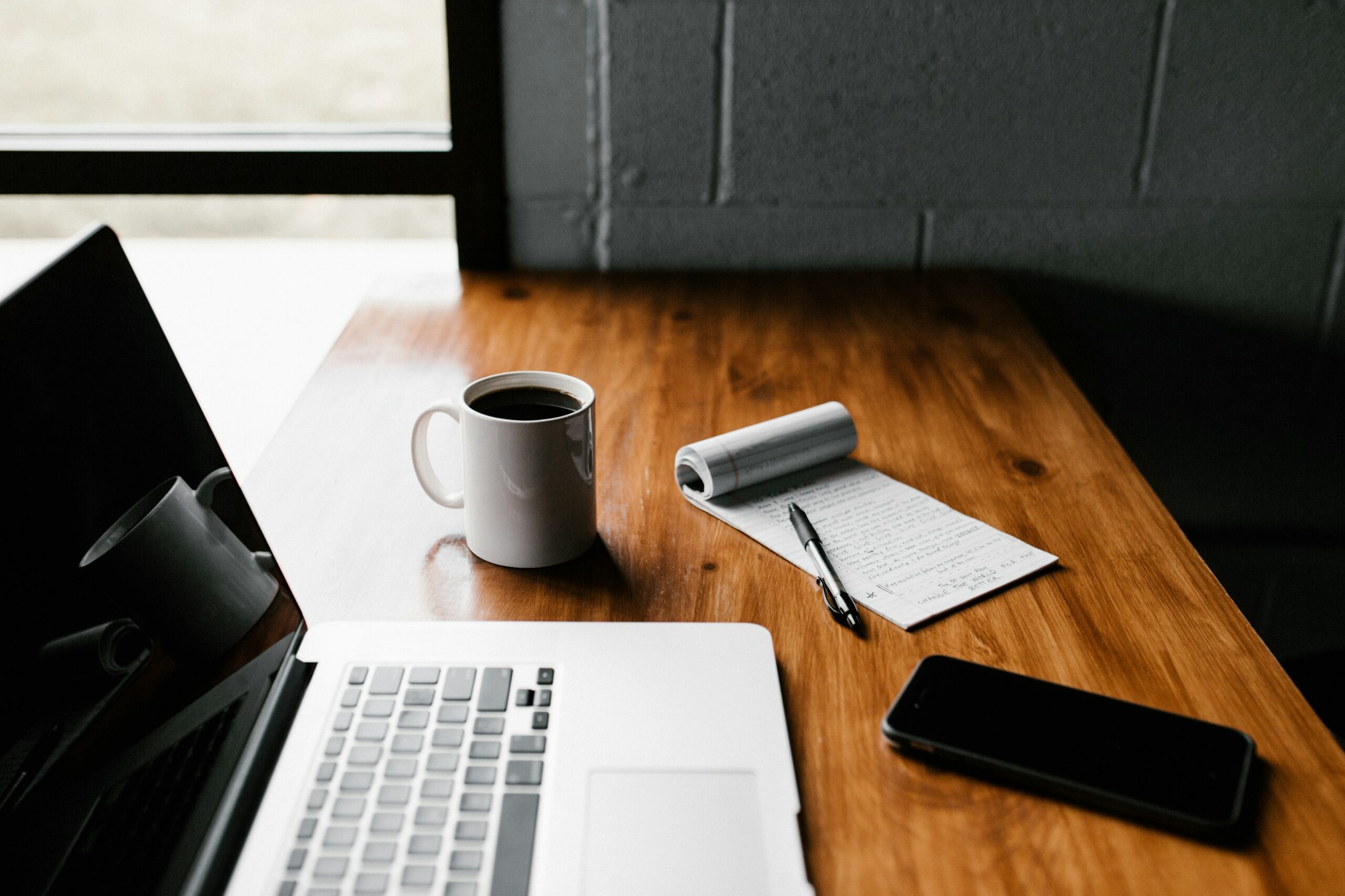Scrivania da lavoro con laptop, tazza di caffè e taccuino, atmosfera di concentrazione