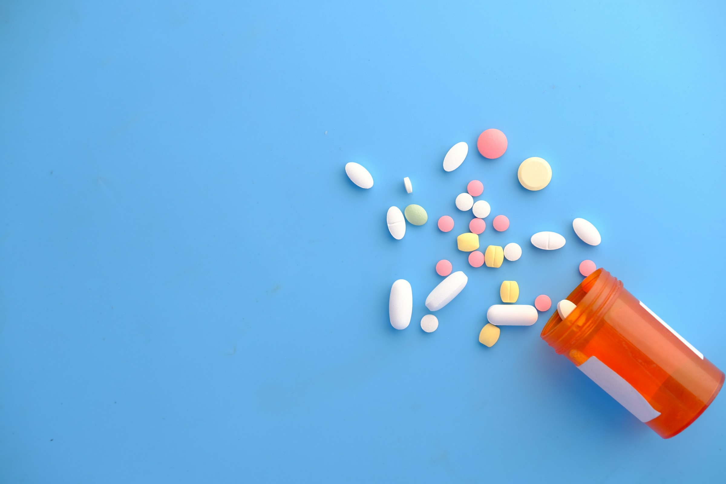 Flacone di integratori con compresse colorate rovesciate su un piano