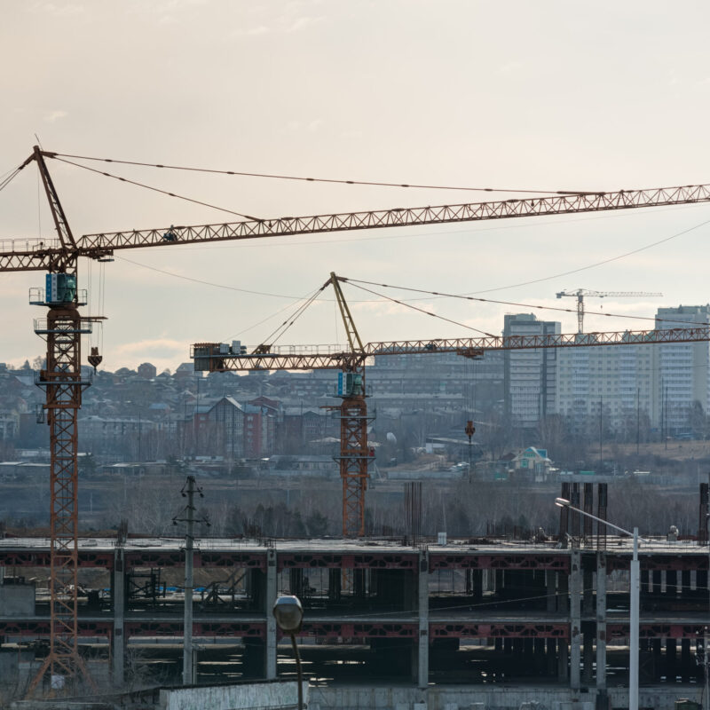 Due gru a torre in un cantiere edile al tramonto, silhouette contro il cielo dorato