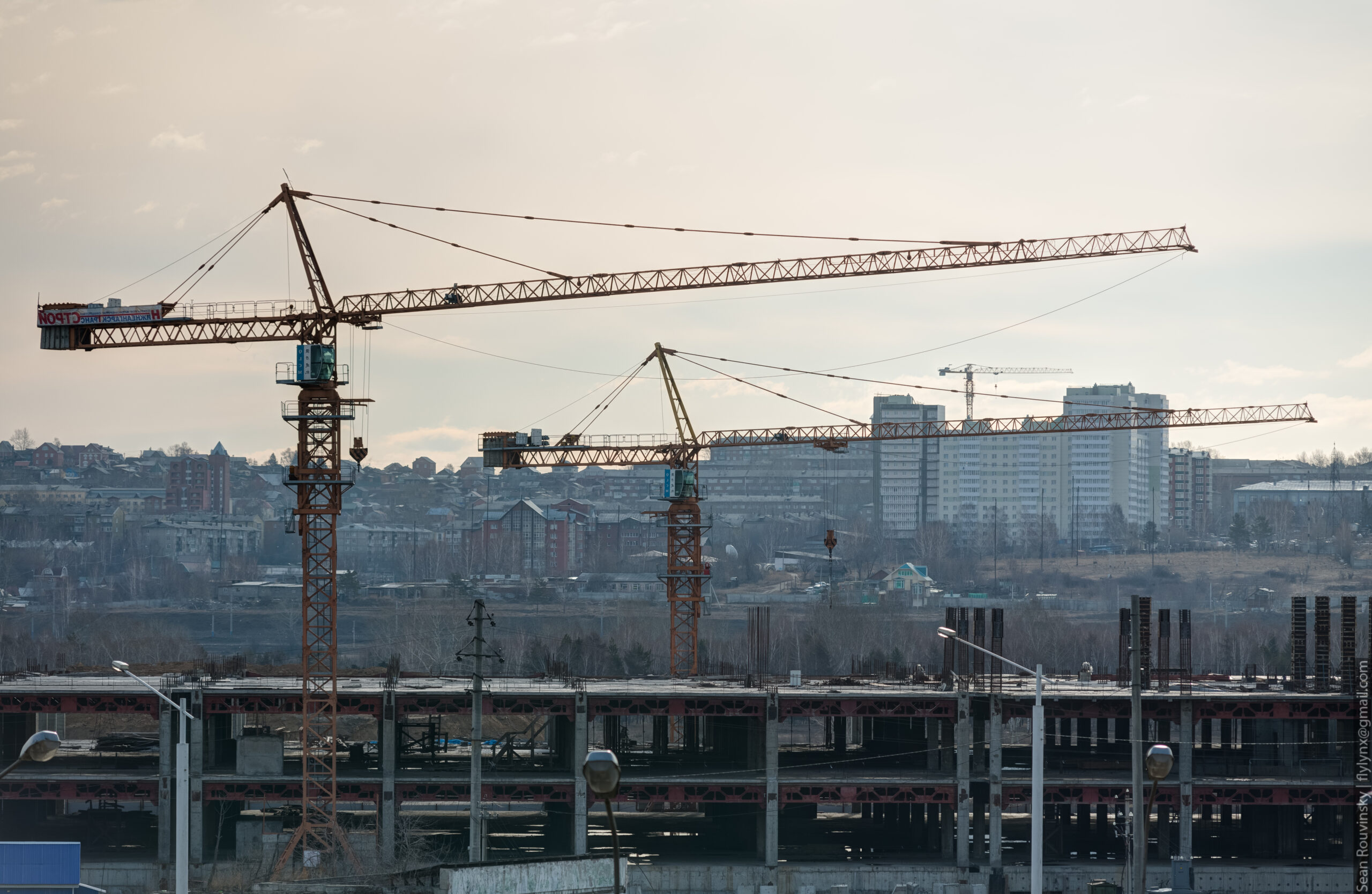 Due gru a torre in un cantiere edile al tramonto, silhouette contro il cielo dorato
