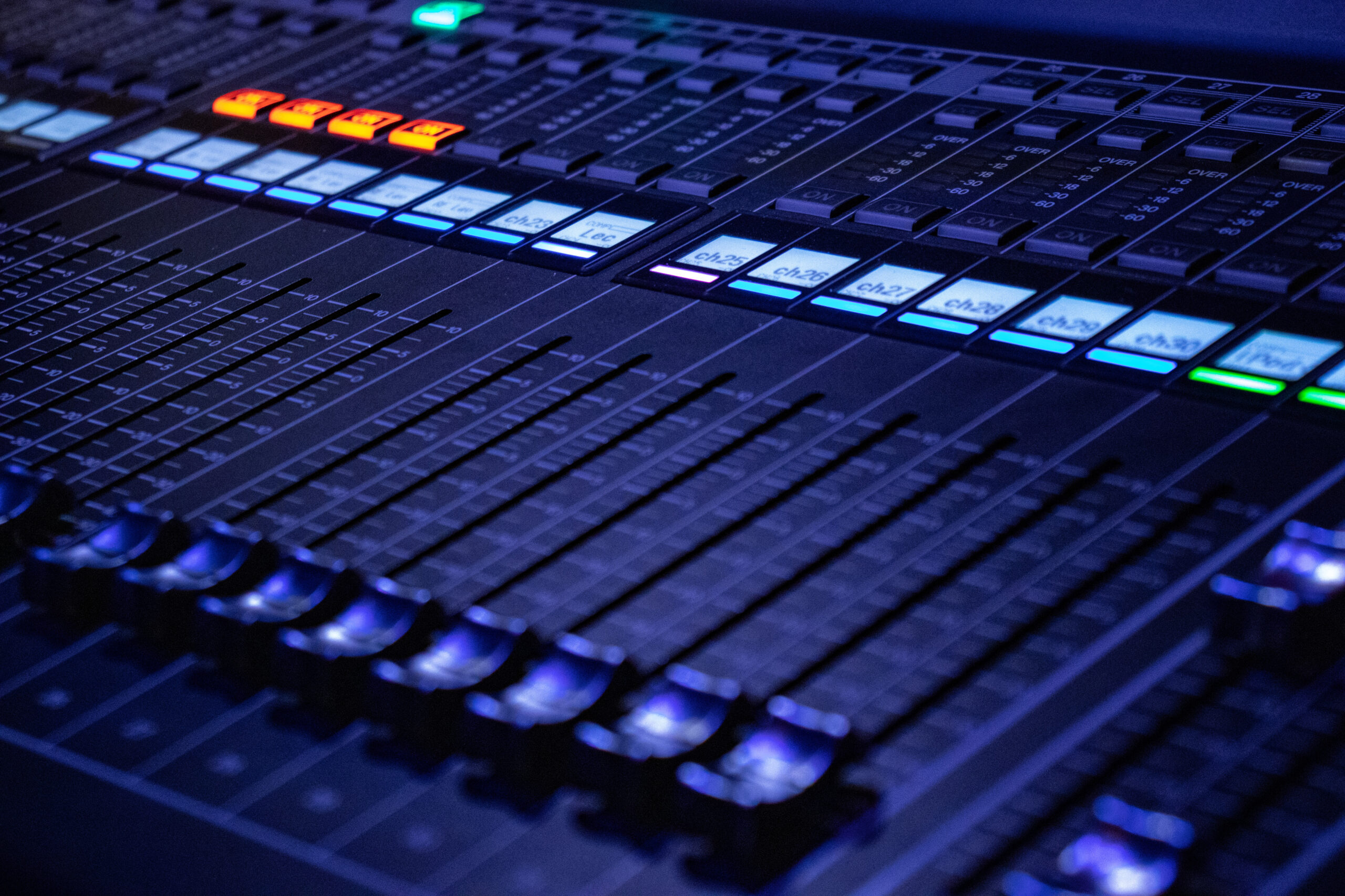 Primo piano di un mixer audio con cursori e pulsanti illuminati durante un evento live