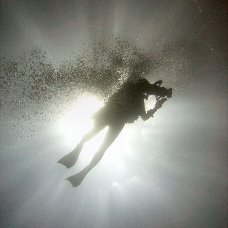 Sagoma di un subacqueo in immersione controluce, circondato da bollicine