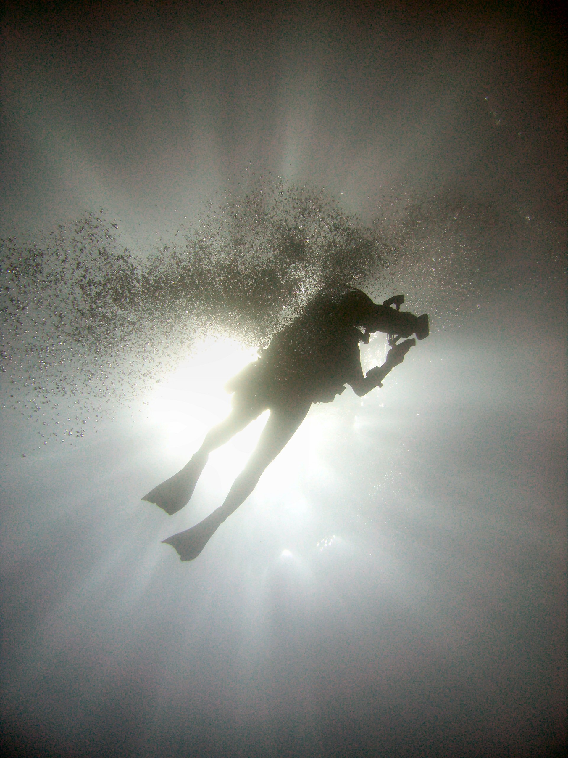 Sagoma di un subacqueo in immersione controluce, circondato da bollicine