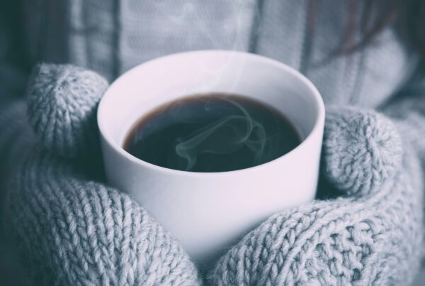 Mani che si scaldano con una tazza calda in inverno