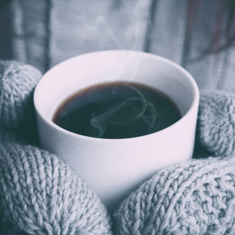 Mani che si scaldano con una tazza calda in inverno