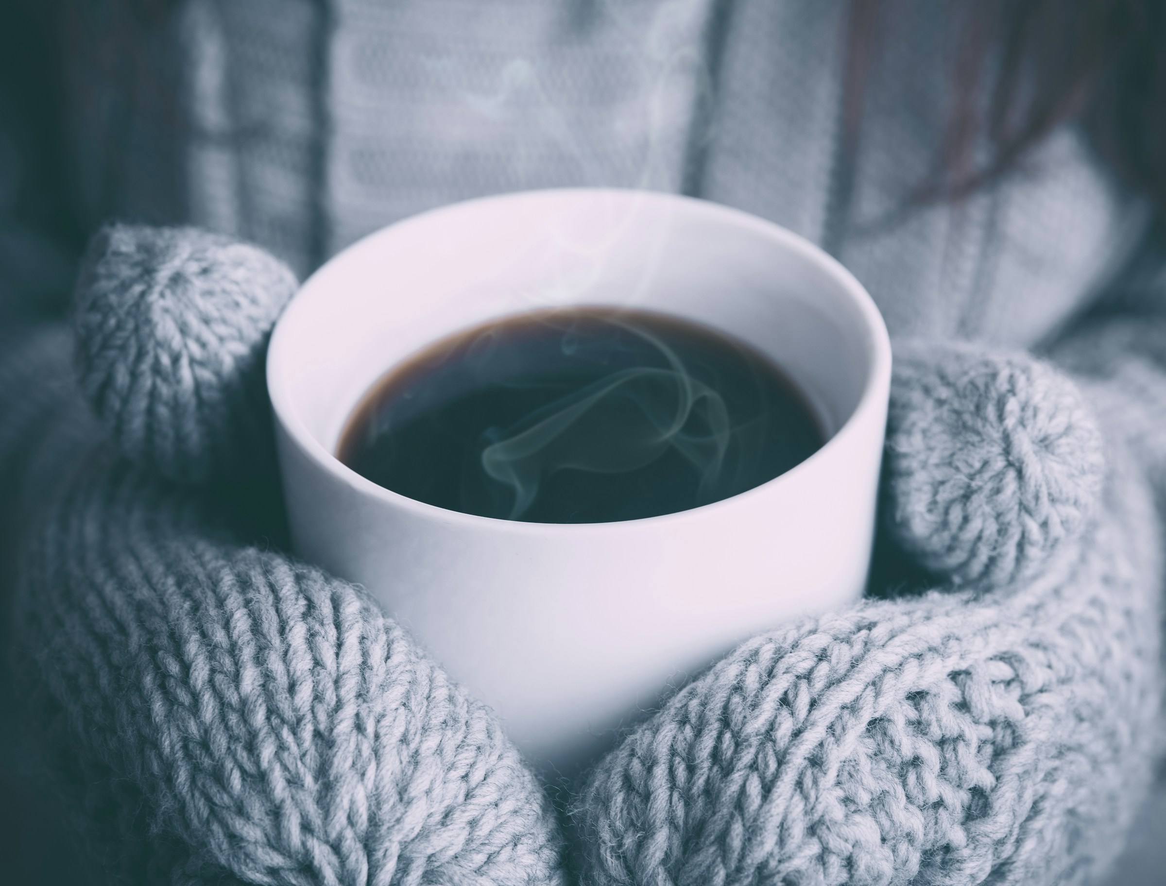 Mani che si scaldano con una tazza calda in inverno
