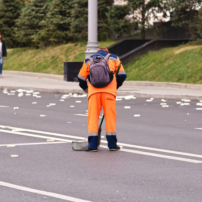Operatore ecologico con divisa ad alta visibilità che pulisce una strada al mattino