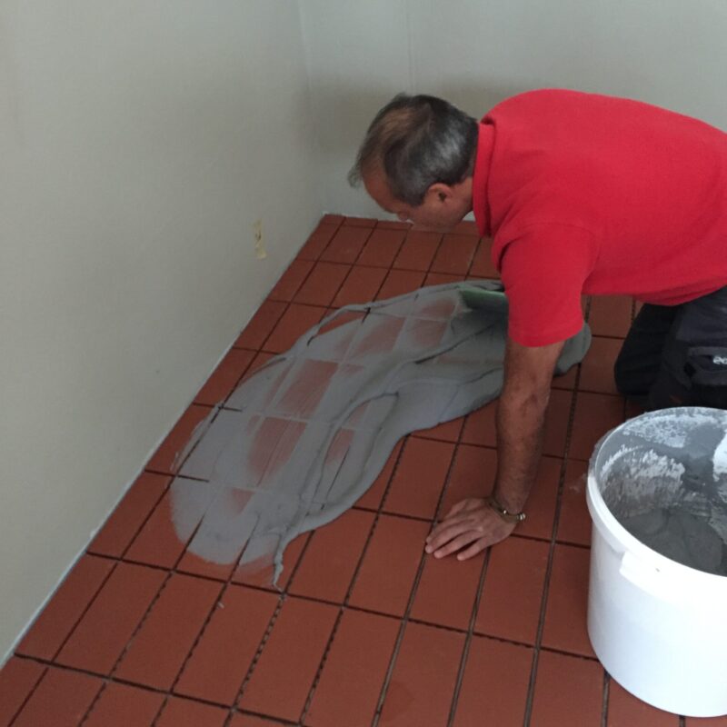 Piastrellista inginocchiato mentre stucca le fughe di un pavimento in cotto con malta cementizia