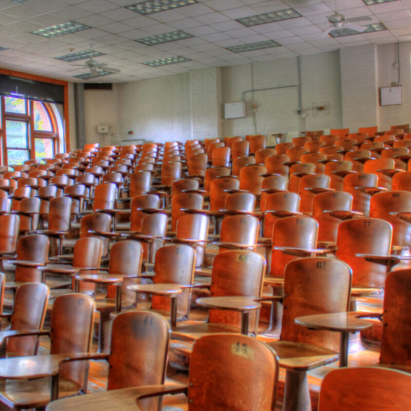 Aula universitaria vuota con file di sedute in legno, vista dal podio del relatore