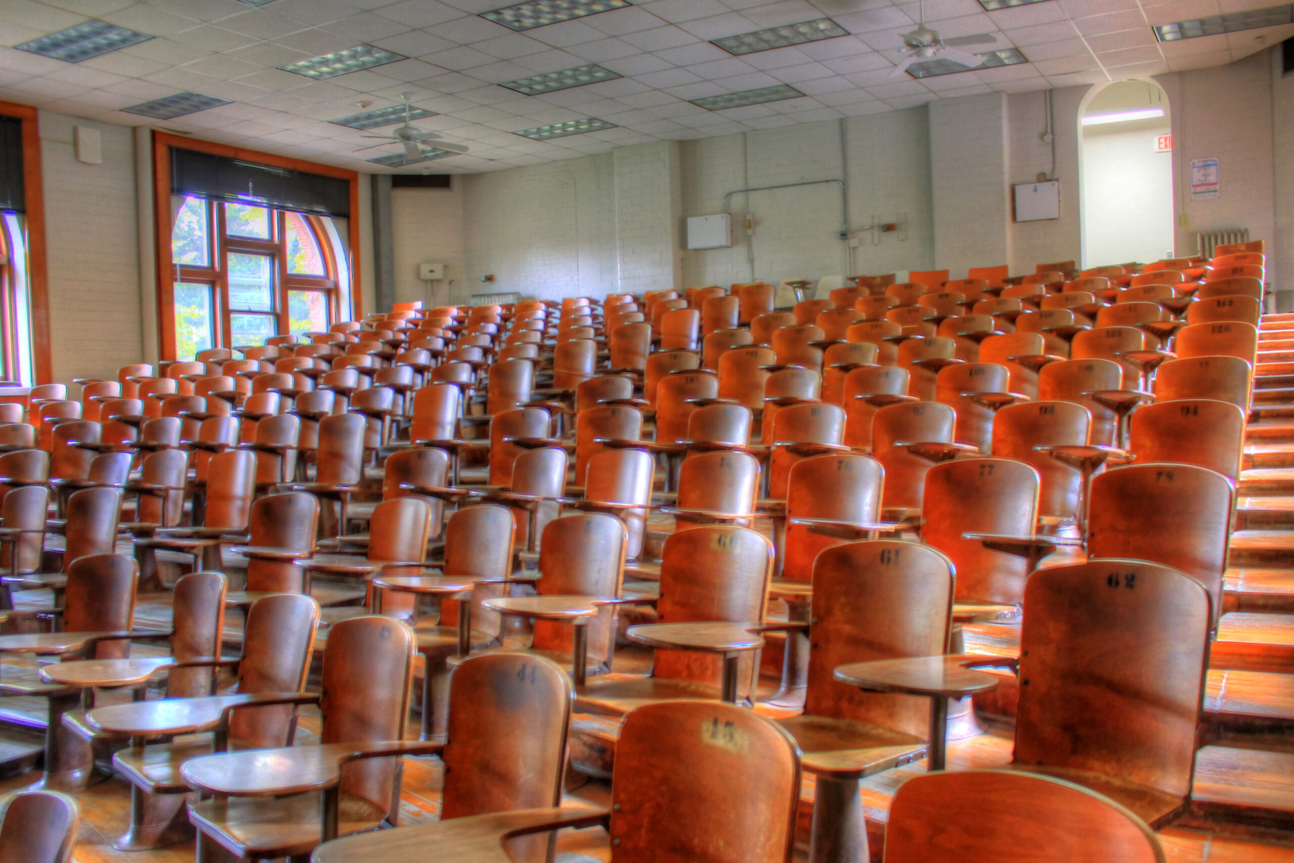 Aula universitaria vuota con file di sedute in legno, vista dal podio del relatore