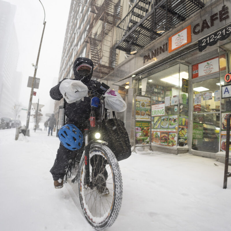 Rider in bicicletta consegna cibo a domicilio durante una tempesta di neve in città