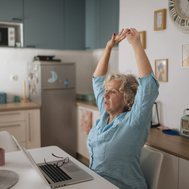 Donna che si stira alla scrivania mentre lavora al computer