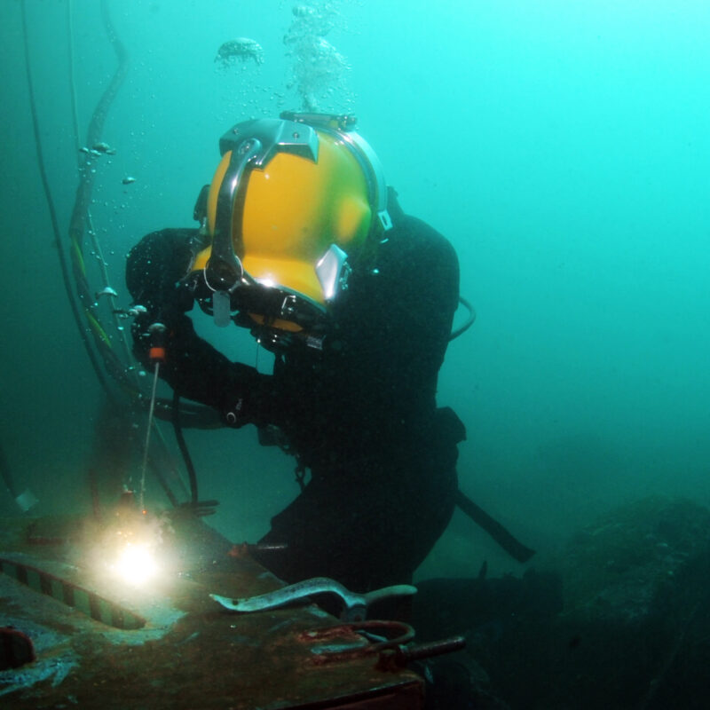Sommozzatore professionista con casco da palombaro esegue una saldatura subacquea su una struttura