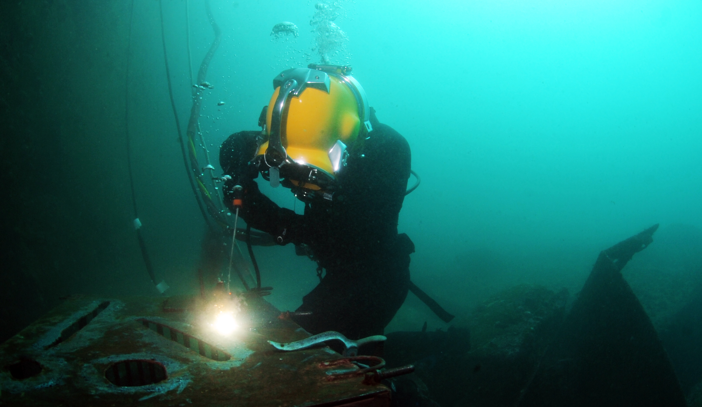 Sommozzatore professionista con casco da palombaro esegue una saldatura subacquea su una struttura