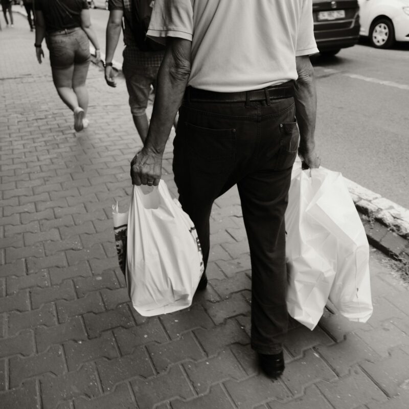 Persona che cammina per strada portando due borse della spesa pesanti