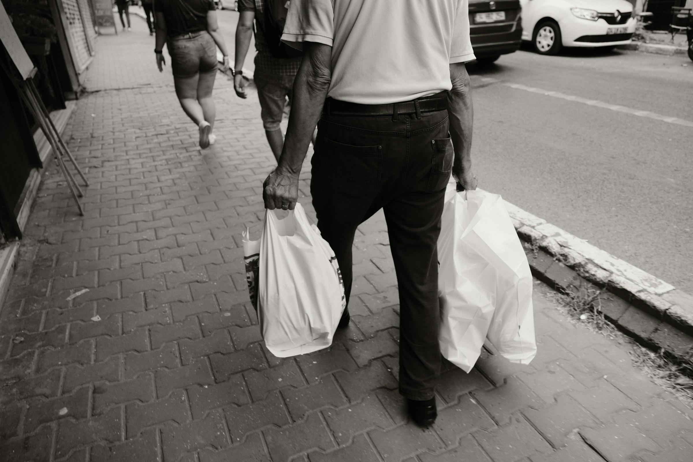 Persona che cammina per strada portando due borse della spesa pesanti