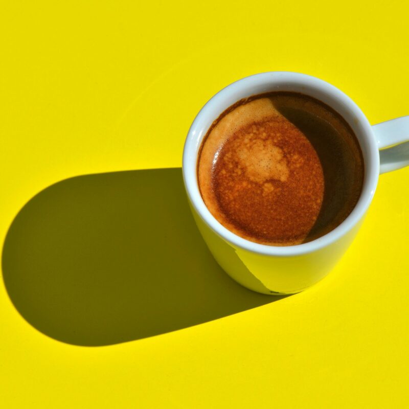 Tazzina di caffè espresso su sfondo giallo acceso, luce del mattino