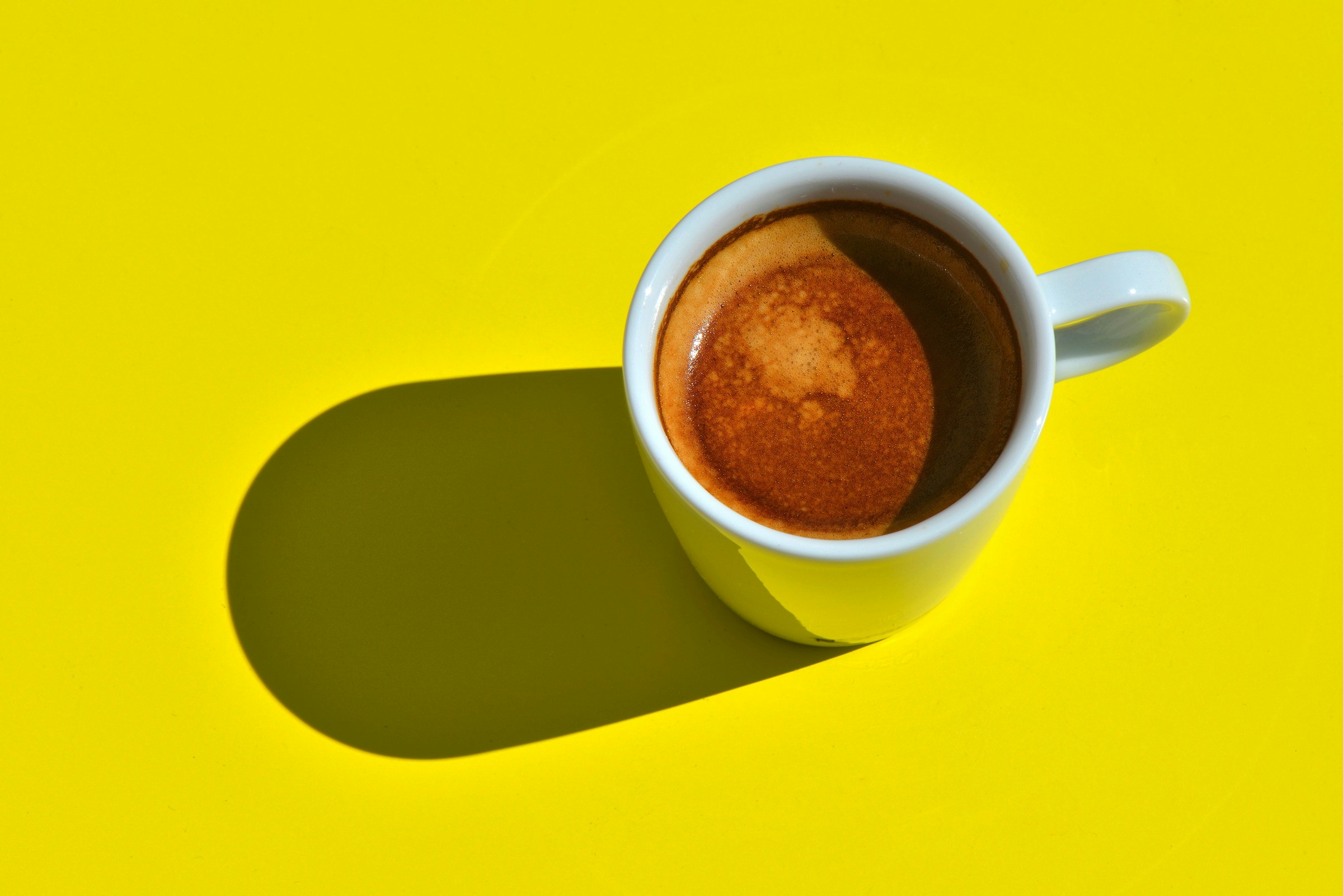 Tazzina di caffè espresso su sfondo giallo acceso, luce del mattino