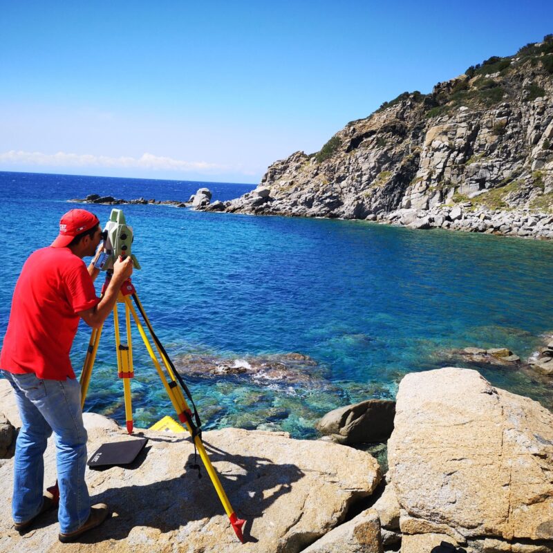 Topografo con stazione totale su treppiede esegue un rilievo topografico su una costa rocciosa