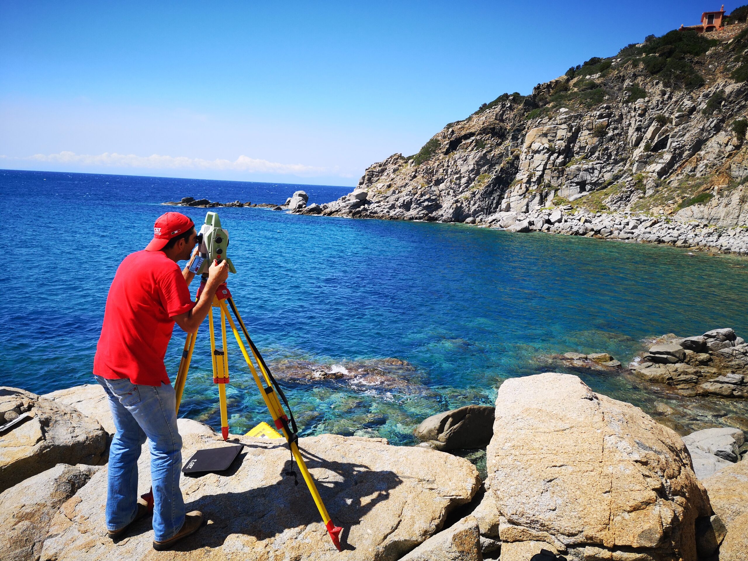 Topografo con stazione totale su treppiede esegue un rilievo topografico su una costa rocciosa