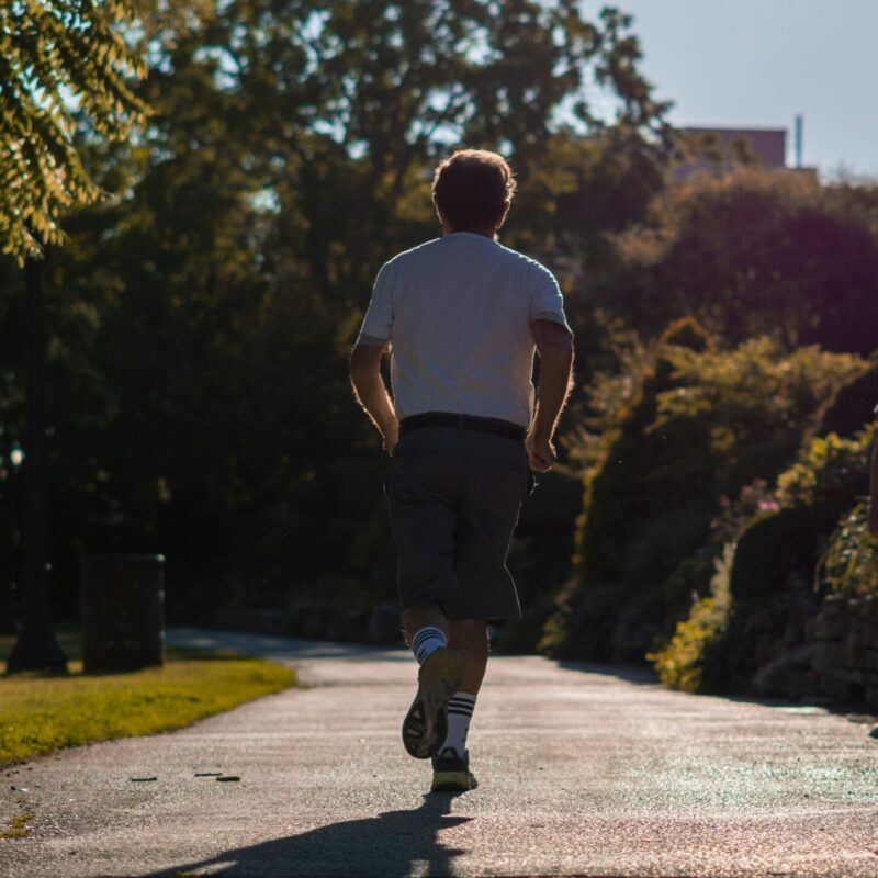 Uomo di spalle mentre corre su un sentiero nel parco in una giornata di sole