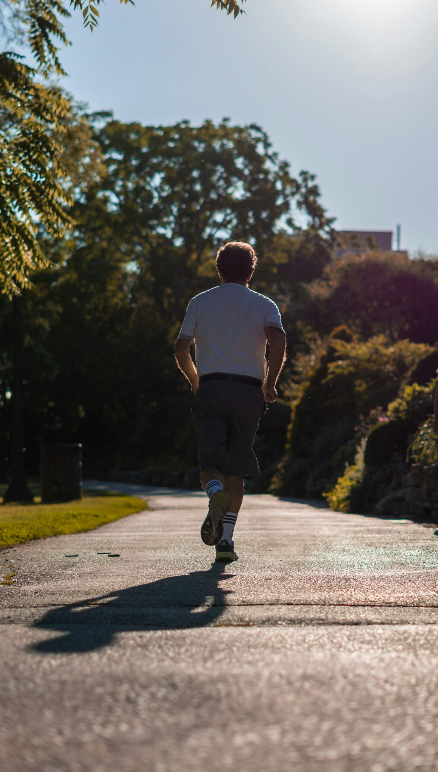Uomo di spalle mentre corre su un sentiero nel parco in una giornata di sole