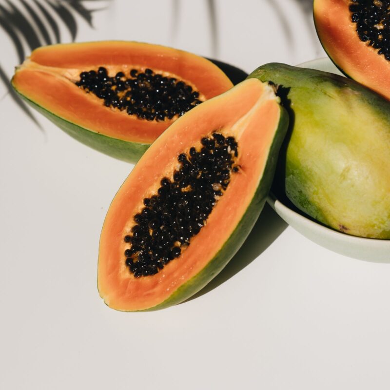 Papaya fresca tagliata a metà su superficie chiara, con semi neri in evidenza