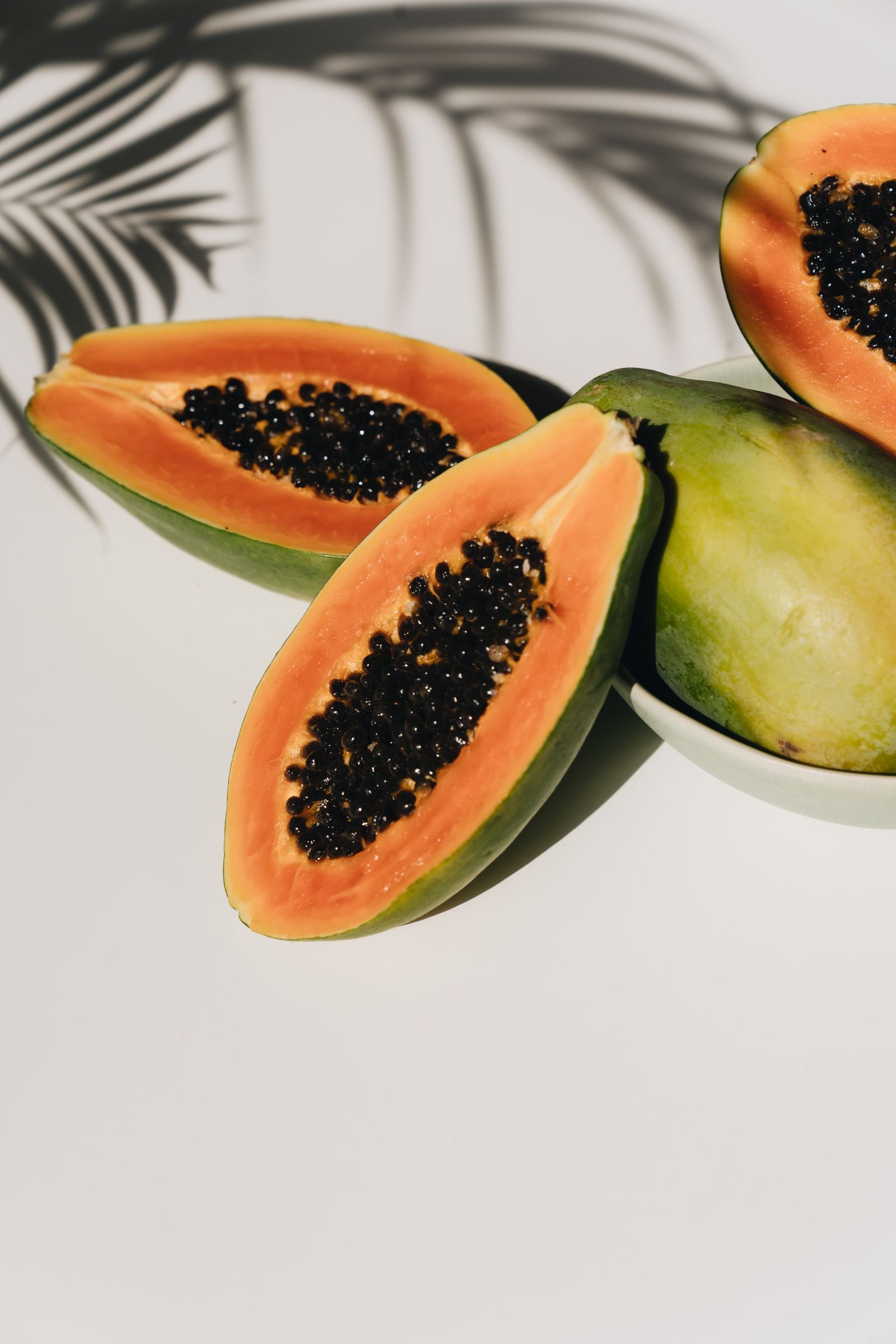 Papaya fresca tagliata a metà su superficie chiara, con semi neri in evidenza