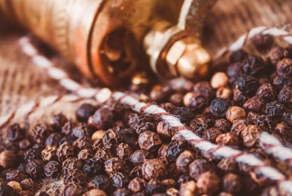 Grani di pepe nero accanto a un macinapepe in ottone, fonte naturale di piperina