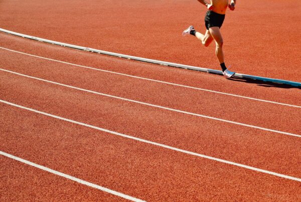 Atleta corre su pista rossa allo stadio in una giornata di sole, immagine su taurina e sport