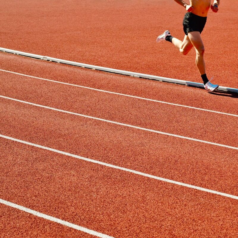 Atleta corre su pista rossa allo stadio in una giornata di sole, immagine su taurina e sport