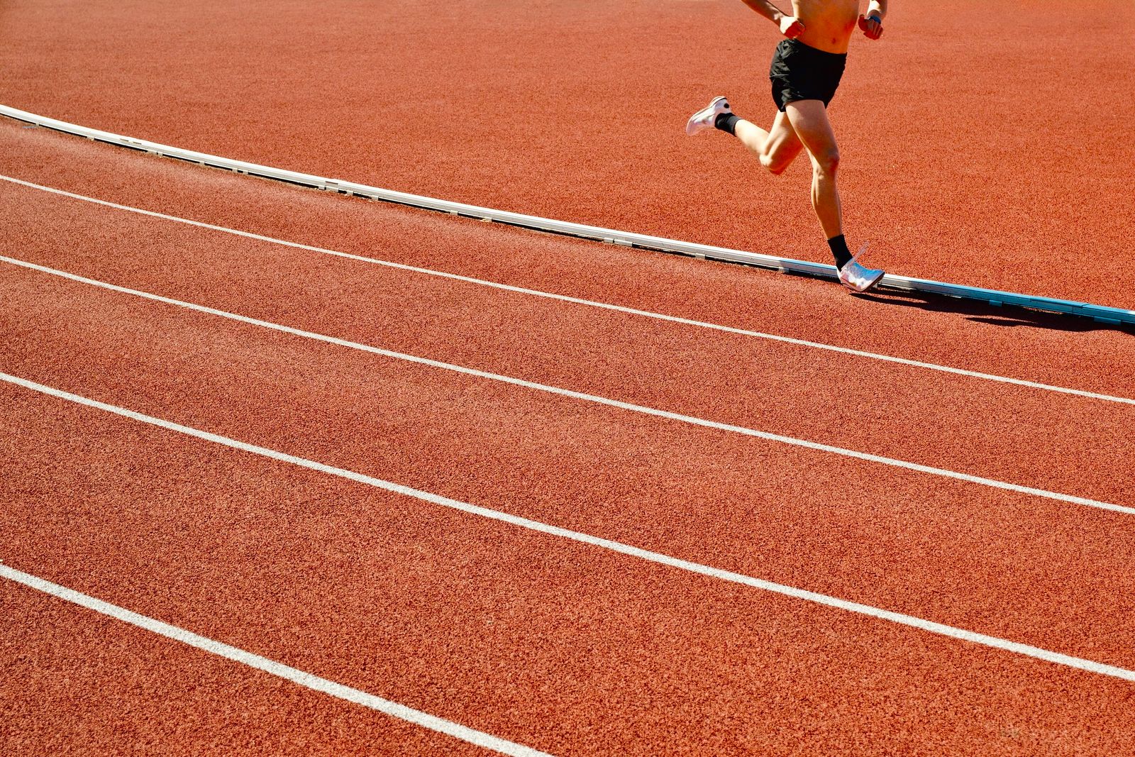 Atleta corre su pista rossa allo stadio in una giornata di sole, immagine su taurina e sport