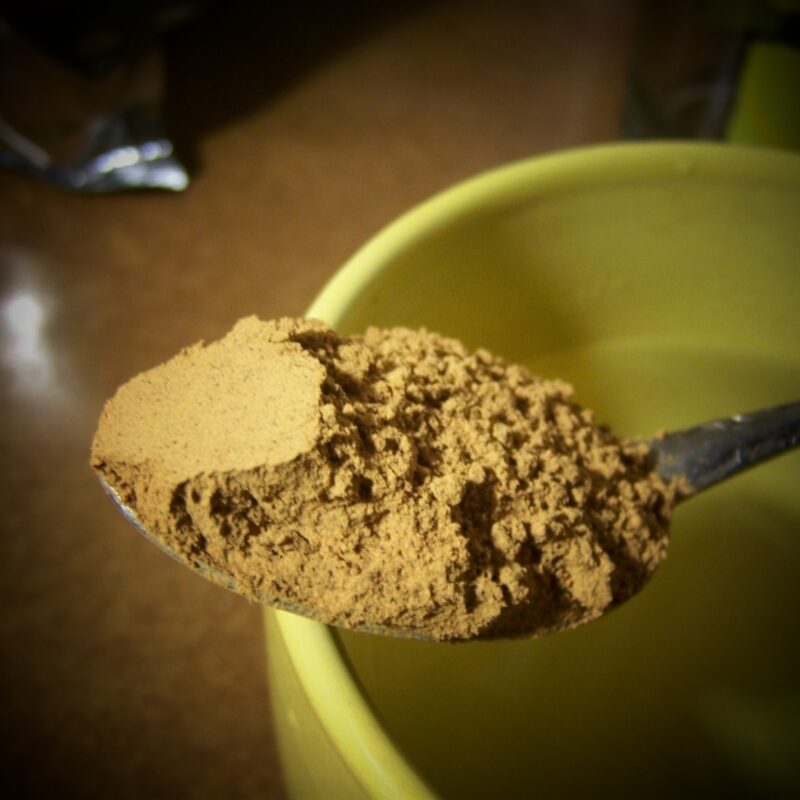 Cucchiaio con polvere marrone di guaranà, davanti a una tazza gialla