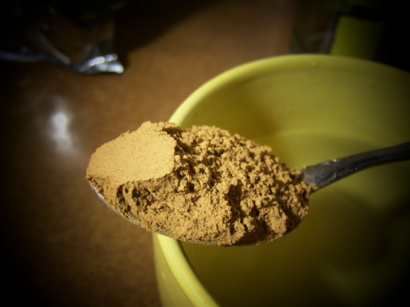 Cucchiaio con polvere marrone di guaranà, davanti a una tazza gialla