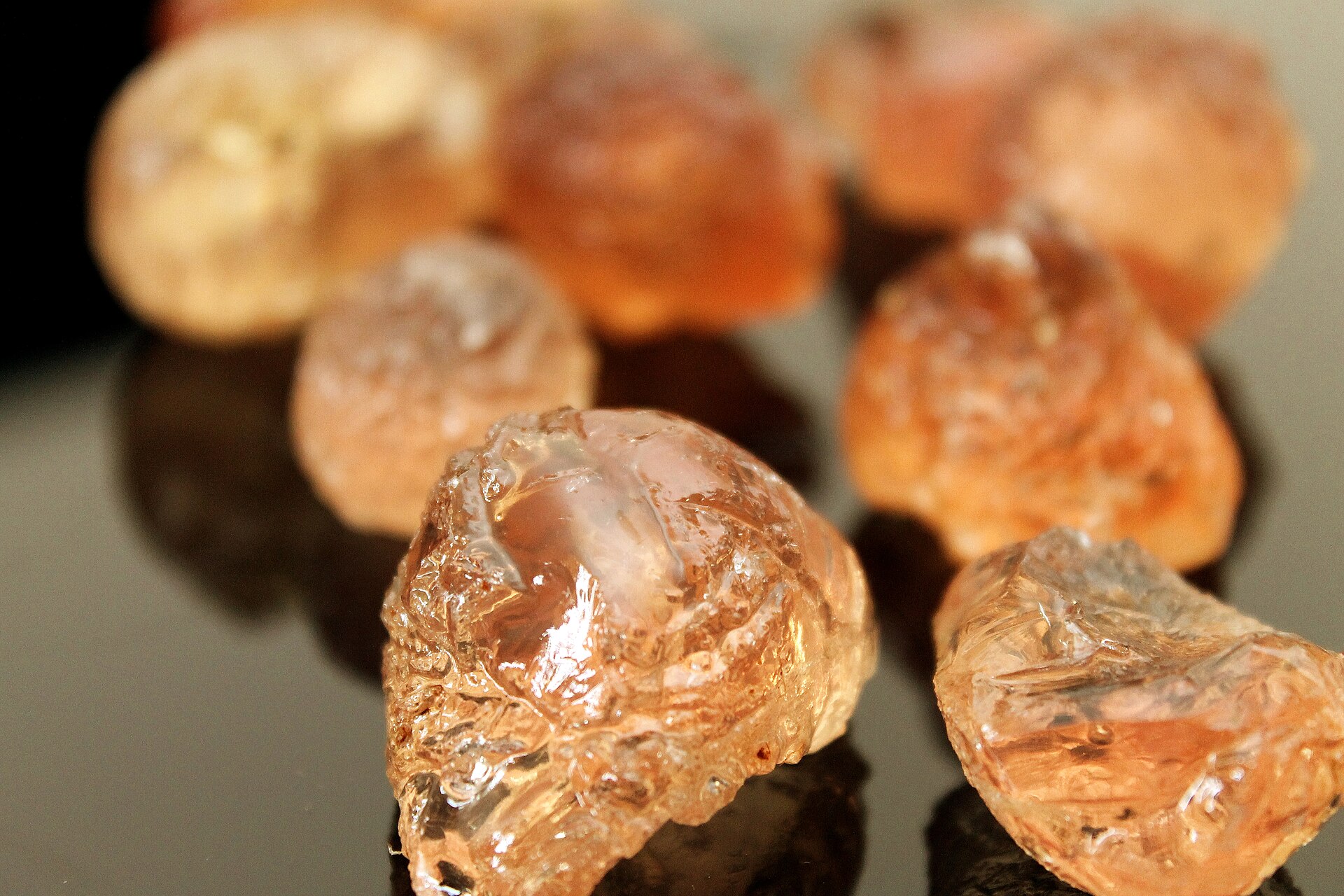 Grumi traslucidi di gomma arabica grezza, di colore ambrato, appoggiati su una superficie scura e lucida