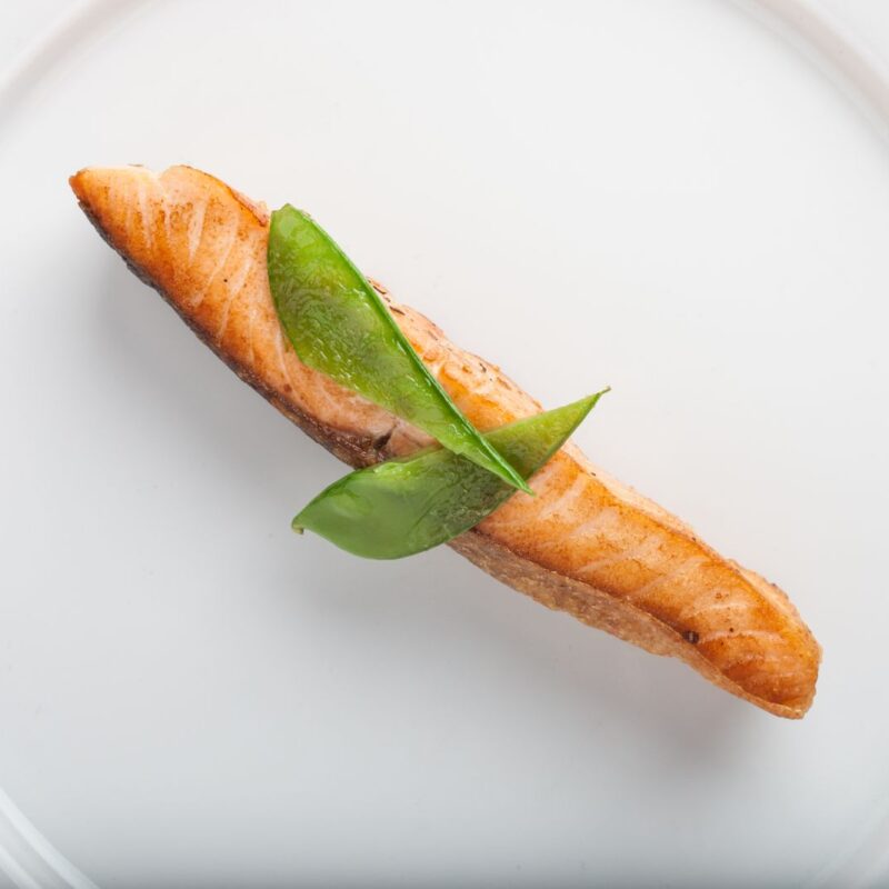 Filetto di salmone cotto con guarnizione verde su un piatto bianco, alimento che contiene omega-3