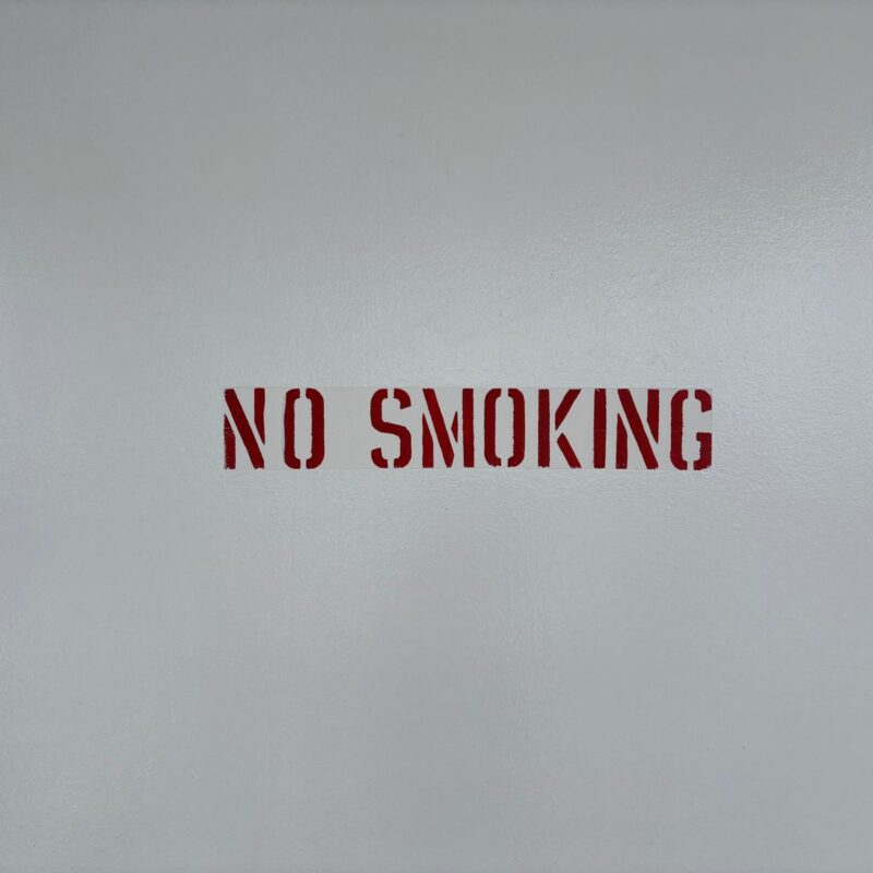 Scritta rossa NO SMOKING su una parete grigia, simbolo di ambiente senza fumo