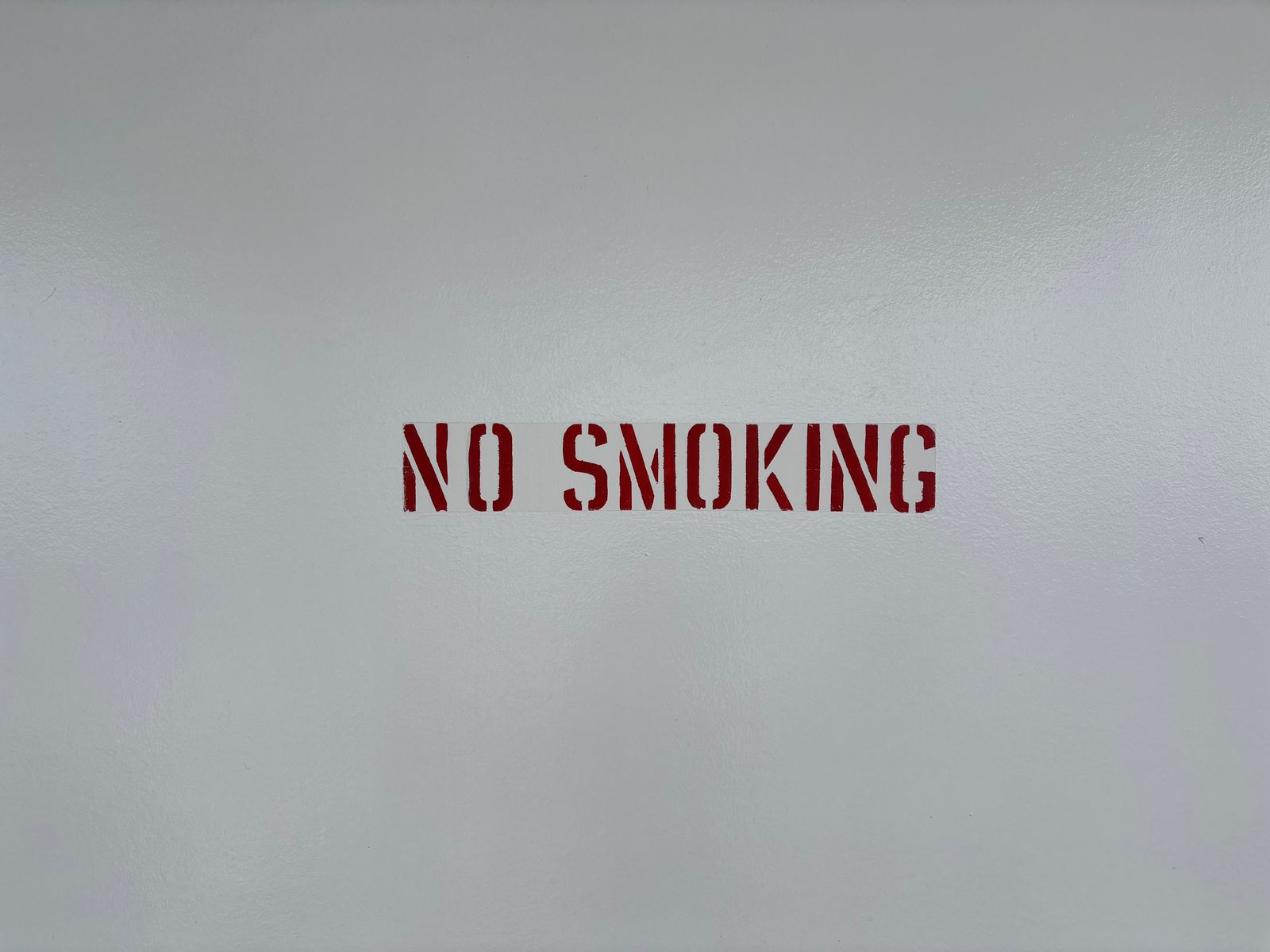 Scritta rossa NO SMOKING su una parete grigia, simbolo di ambiente senza fumo